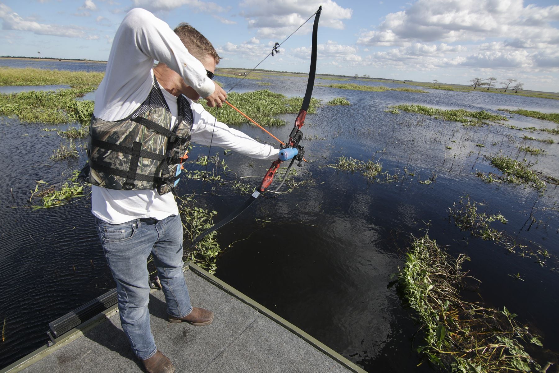 Bowfisher on a flat-bottom boat in shallow marsh water during the day