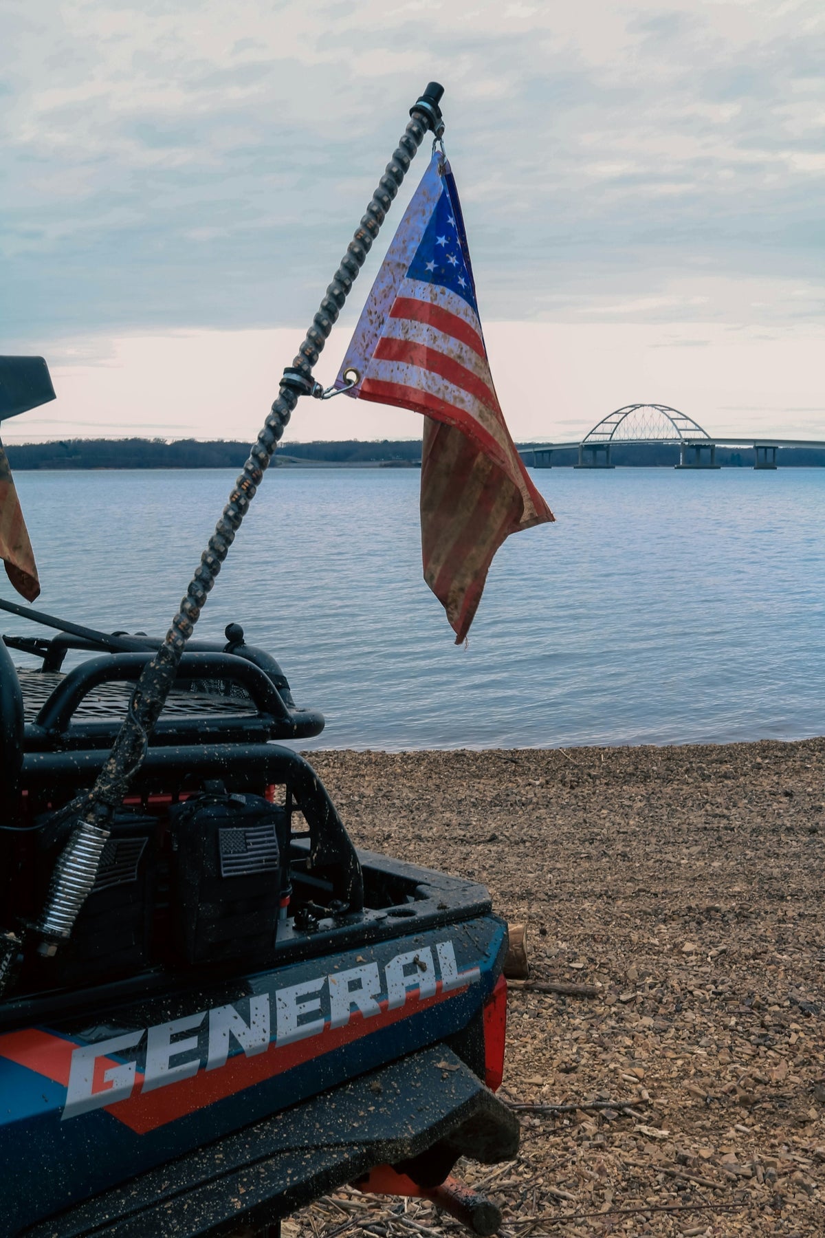 Off-road vehicle with American flag parked beside a lake, symbolizing outdoor freedom and hunting adventures.